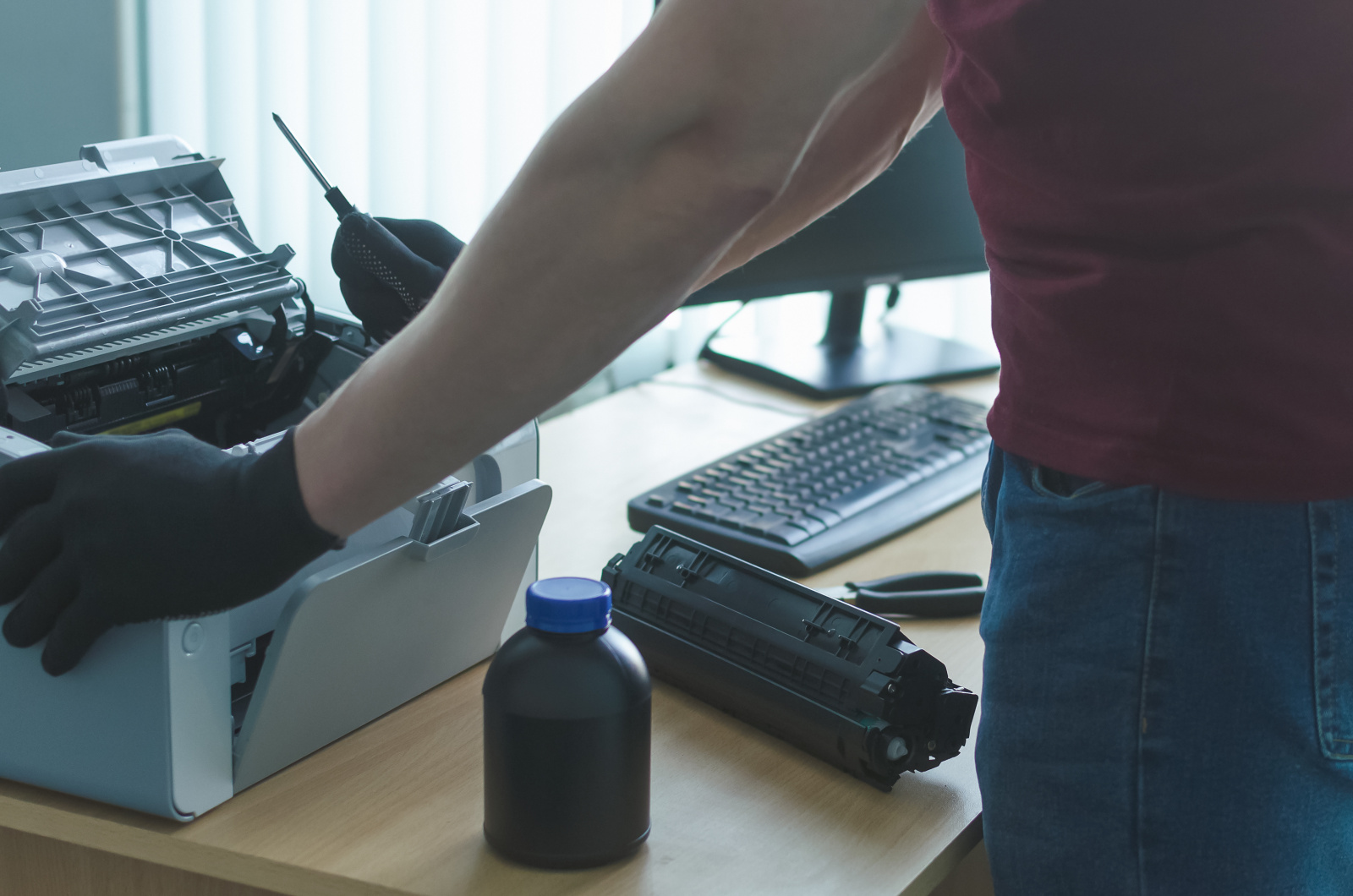 Muž vyměňující toner v laserové tiskárně se šroubovákem v ruce.